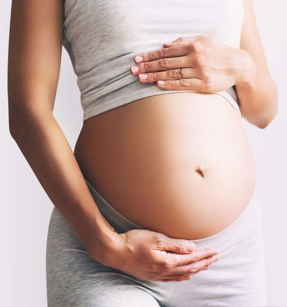 Pregnant woman gently holding her baby bump during prenatal wellness care